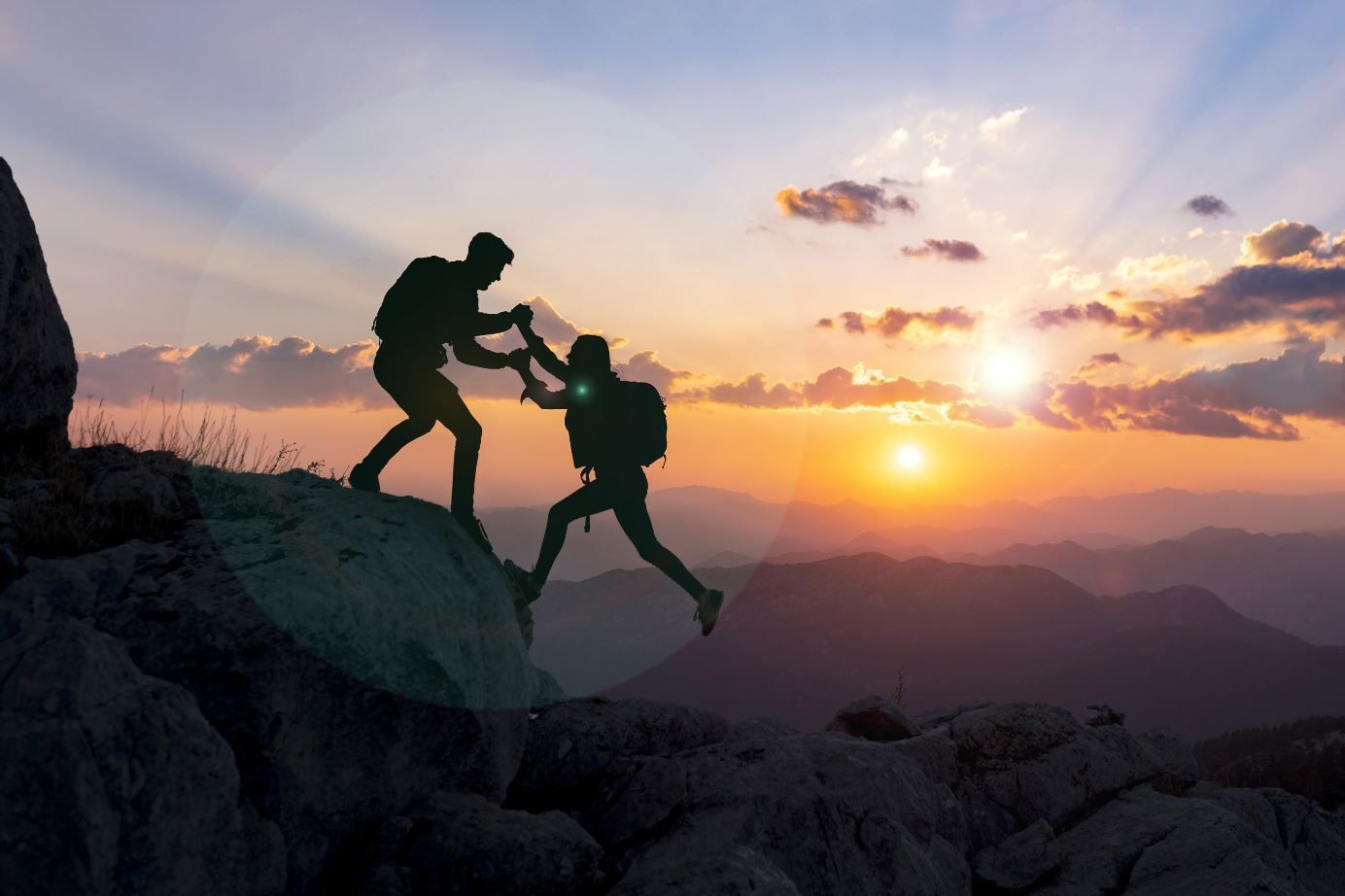 Silhouettes de deux personnes s’entraidant pour gravir un sommet au coucher du soleil